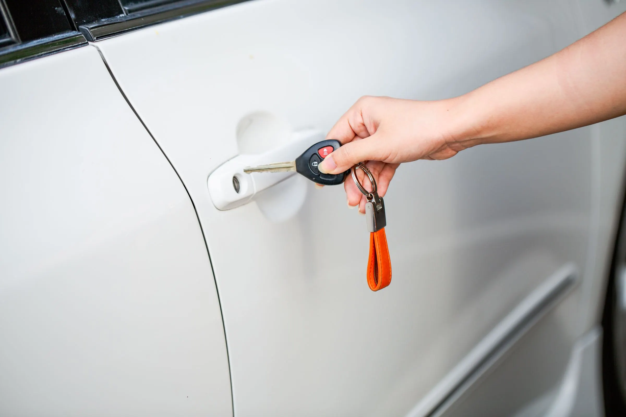 Hand schließt mit einem Schlüssel eine weiße Autotür auf